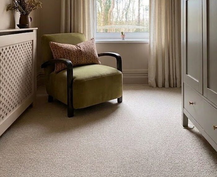 A green chair in the corner of a small room containing beige carpet.