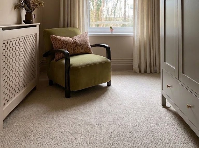 A green chair in the corner of a small room containing beige carpet.